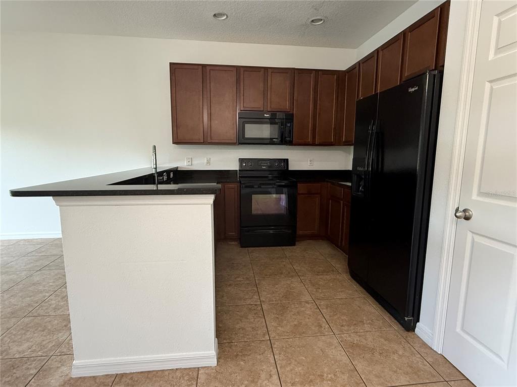 A kitchen features dark wood cabinets, black appliances, and a breakfast bar with dark countertops — 12243 CITRUSWOOD DRIVE, ORLANDO, FL