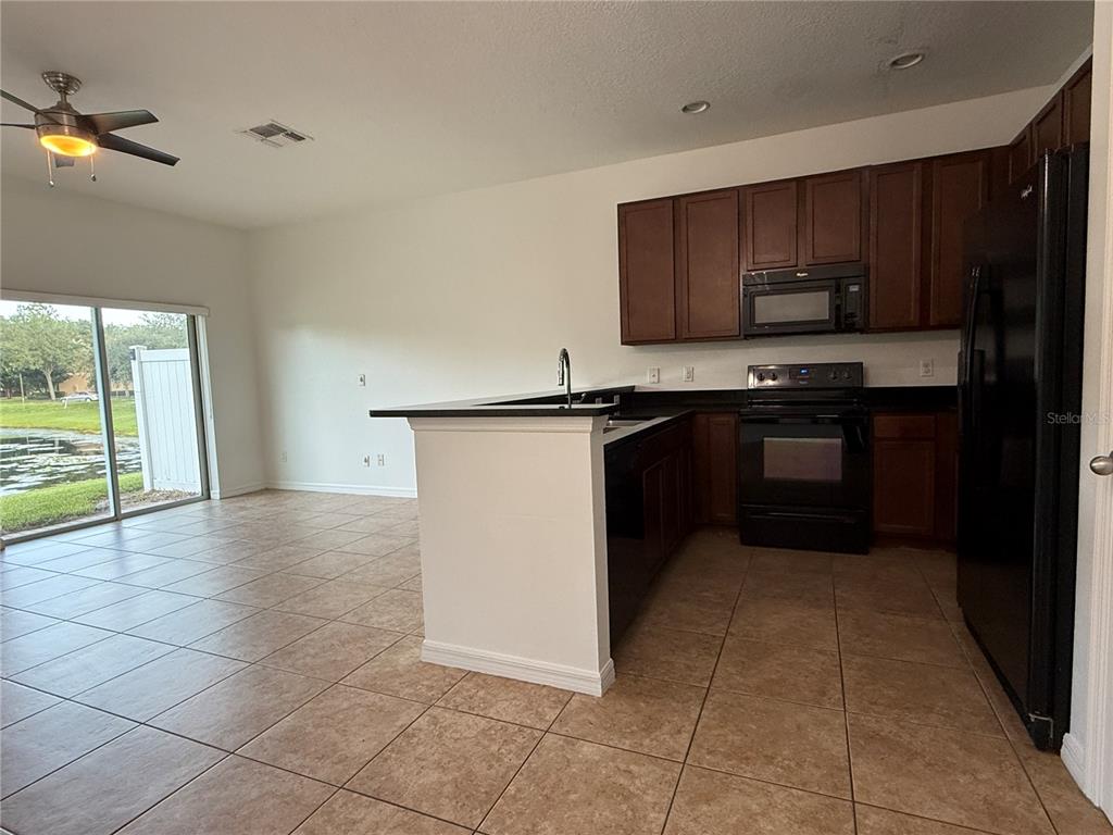 A kitchen with dark wood cabinets, black appliances, and tile flooring opens to a living area — 12243 CITRUSWOOD DRIVE, ORLANDO, FL