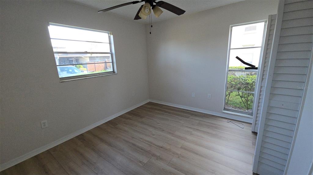 An empty bedroom features light wood-look flooring, a ceiling fan, and two windows — 4849 ONYX LANE UNIT 101, NEW PORT RICHEY, FL