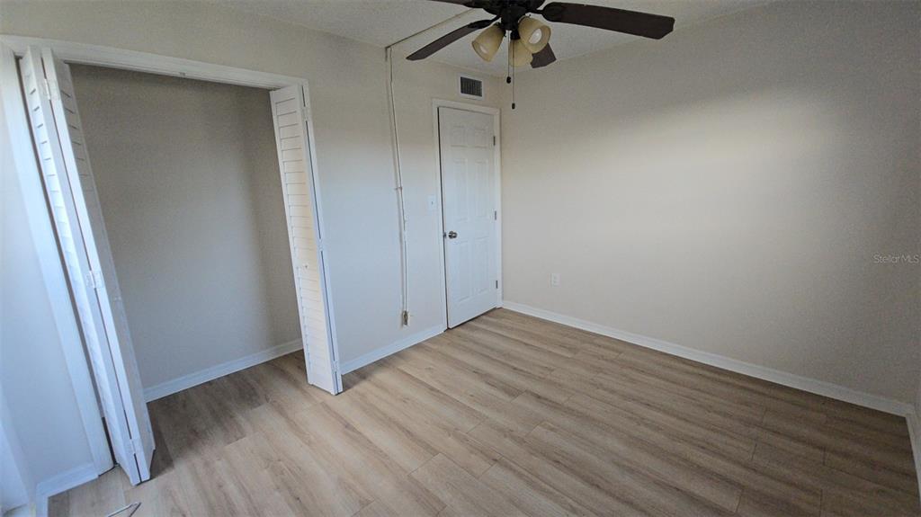 An empty bedroom features light wood-look flooring, a ceiling fan, and a white closet — 4849 ONYX LANE UNIT 101, NEW PORT RICHEY, FL