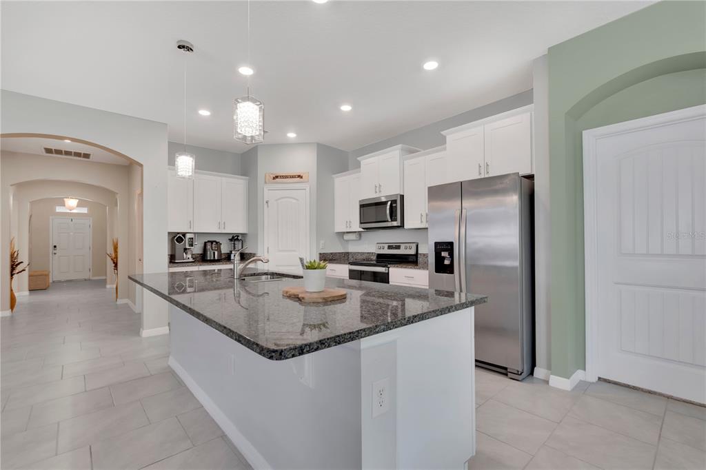 A kitchen features a granite-topped island, white cabinetry, stainless steel appliances, and light tile flooring — 1621 PARK SIDE AVENUE, KISSIMMEE, FL