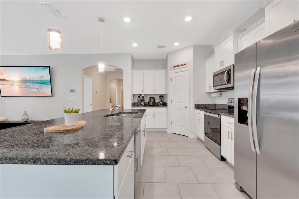 A modern kitchen features white cabinets, granite countertops, stainless steel appliances, and a large island — 1621 PARK SIDE AVENUE, KISSIMMEE, FL