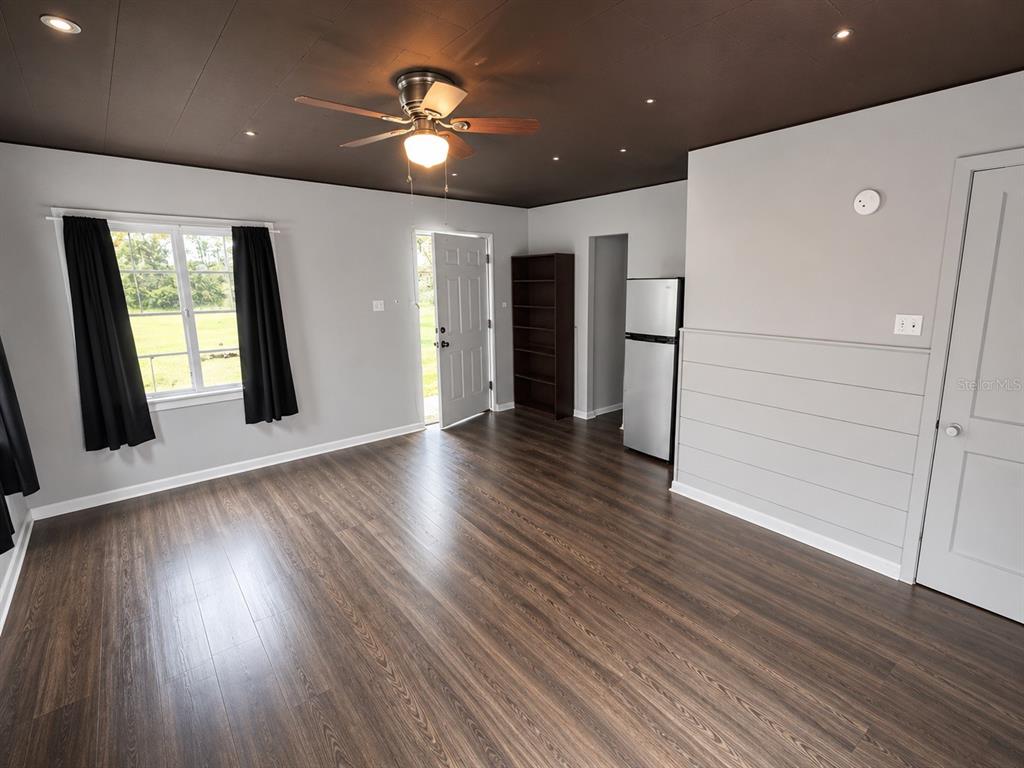 A room with dark wood flooring, a dark ceiling, a ceiling fan, and a refrigerator — 8010 SE US HIGHWAY 301 UNIT 4B, HAWTHORNE, FL