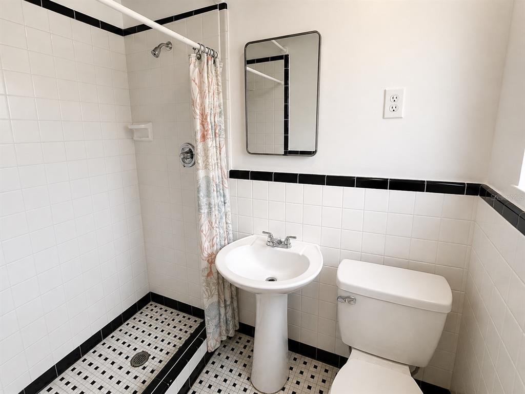 A bathroom features a pedestal sink, a toilet, and a tiled shower with black trim — 8010 SE US HIGHWAY 301 UNIT 4B, HAWTHORNE, FL