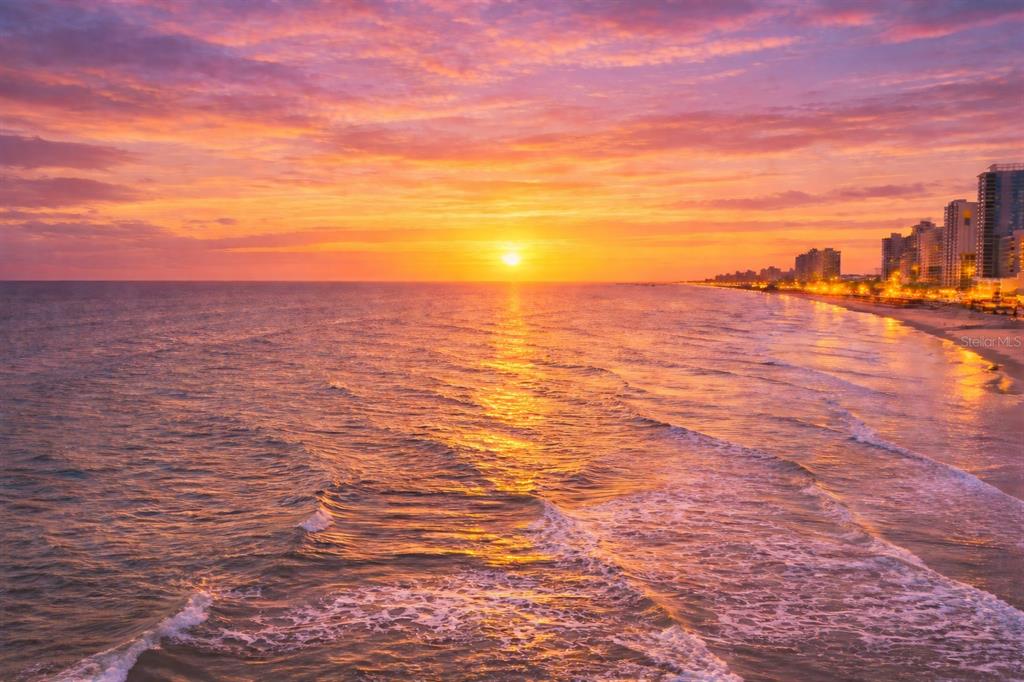 An aerial view of a beach at sunset with a city skyline in the distance — 800 N ATLANTIC AVENUE UNIT 705, DAYTONA BEACH, FL