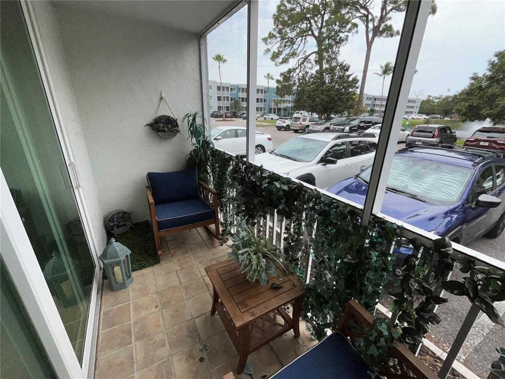 A screened-in balcony features tiled flooring, two chairs, a small table, and artificial greenery — 2700 COCONUT BAY LN LANE UNIT 4111, SARASOTA, FL