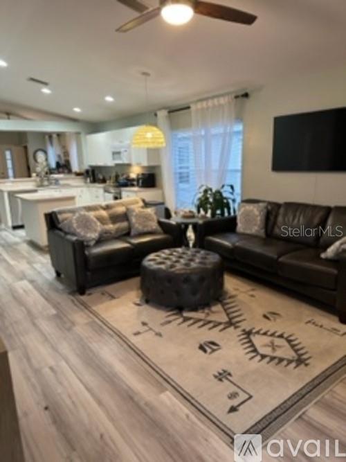 A living room with dark leather sofas, a tufted ottoman, and an open-concept kitchen — 11308 PALM ISLAND AVENUE, RIVERVIEW, FL