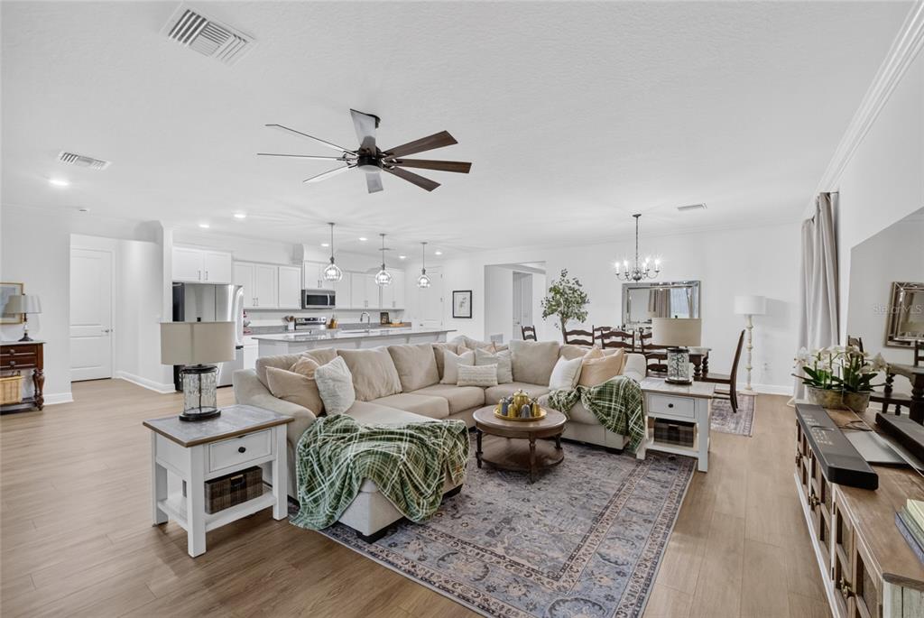 An open-concept living room features a large sectional sofa, wood-look flooring, and a kitchen island — 12377 NW 157TH TERRACE, ALACHUA, FL