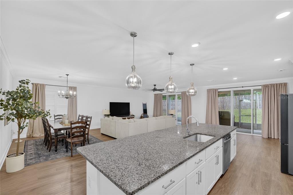 An open-concept kitchen and living area features a granite island, dining table, and sliding doors — 12377 NW 157TH TERRACE, ALACHUA, FL