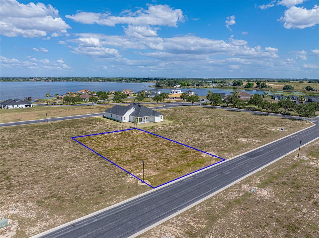 An aerial view shows a vacant rectangular residential lot outlined in blue near a lake — 158 BLAZING STAR AVENUE, LAKE ALFRED, FL