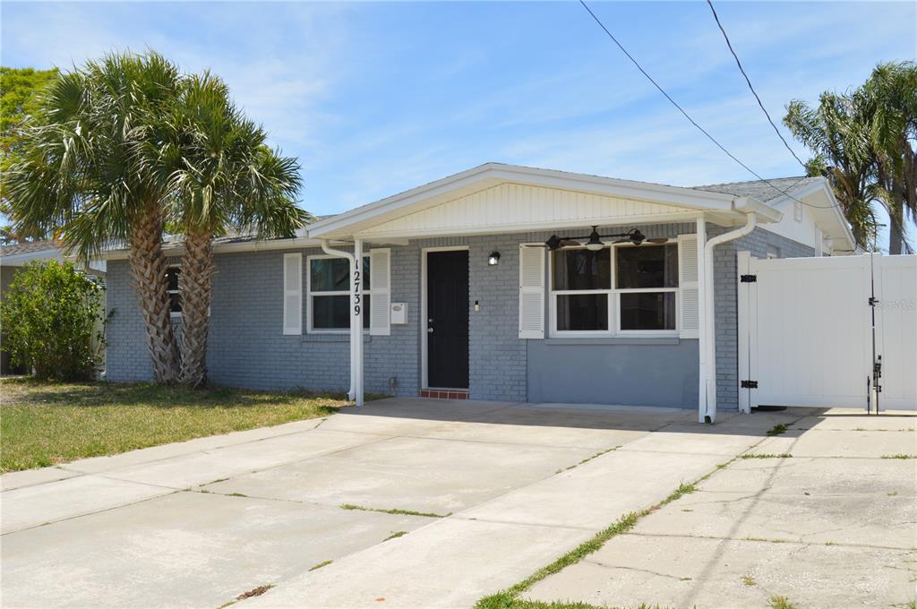 A single-story gray brick house features a white front porch and a concrete driveway — 12739 1ST ISLE, HUDSON, FL