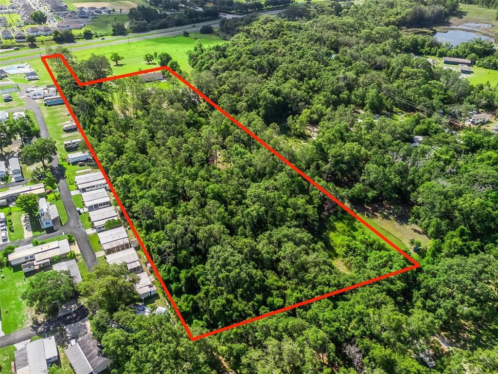 An aerial view shows a rectangular, tree-covered lot outlined in red next to a neighborhood — 26043 US HIGHWAY 27, LEESBURG, FL