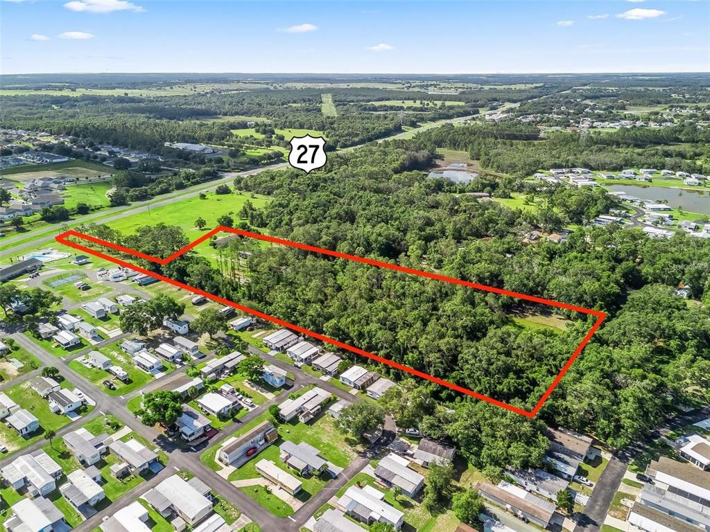 An aerial view shows a rectangular, tree-covered plot of land outlined in red near a highway — 26043 US HIGHWAY 27, LEESBURG, FL