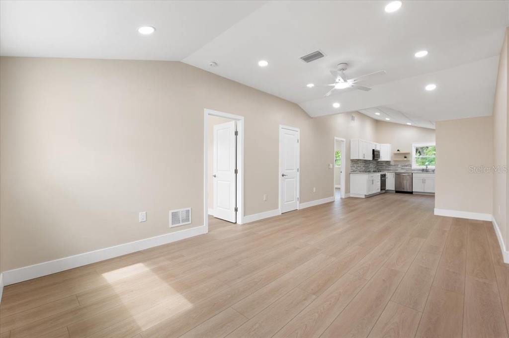 An open-concept living area features light wood-look flooring, vaulted ceilings, and a modern kitchen — 2580 SHAMROCK DRIVE, VENICE, FL