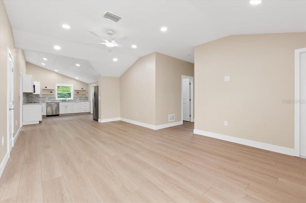 An empty living room features light wood-look flooring, recessed lighting, and a vaulted ceiling — 2580 SHAMROCK DRIVE, VENICE, FL