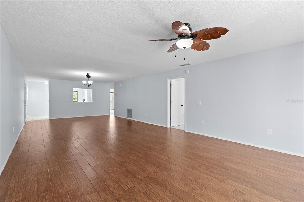 A spacious, empty living room features light gray walls, wood-look flooring, and a ceiling fan — 6110 COUNTRY CLUB WAY UNIT 204, SARASOTA, FL