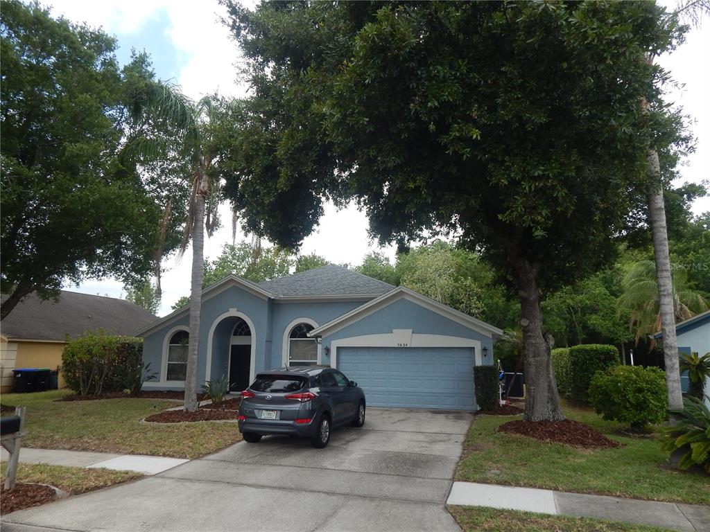 A blue single-story house with a two-car garage and a driveway sits under large trees — 5634 DONNELLY CIRCLE, ORLANDO, FL