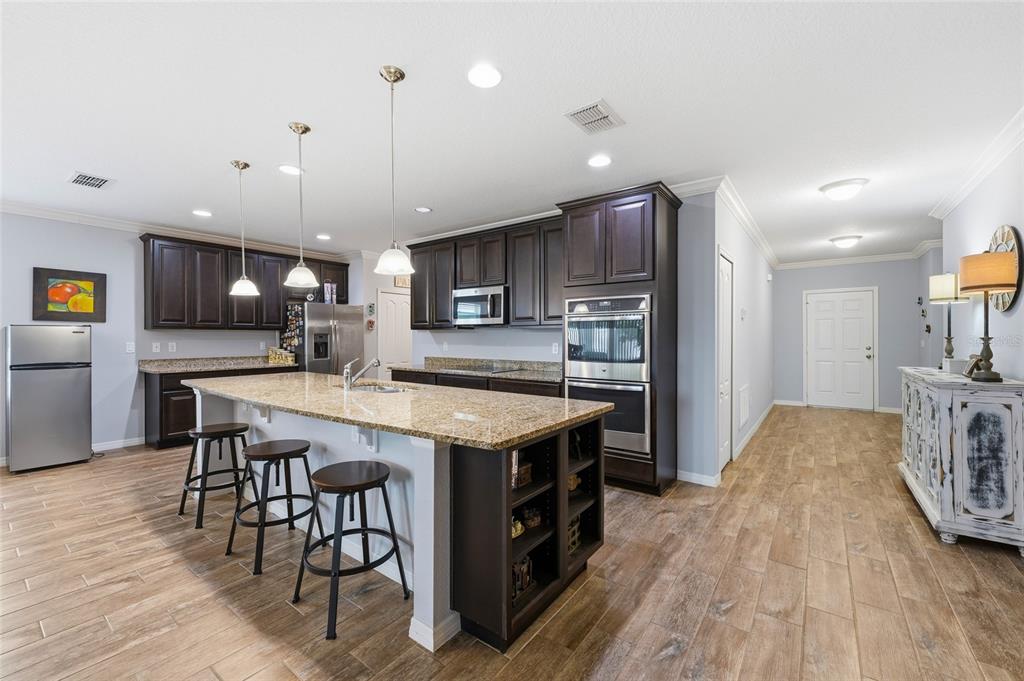 A kitchen features dark wood cabinets, granite countertops, a central island, and wood-look tile flooring — 186 FLATWOODS LOOP, DAVENPORT, FL