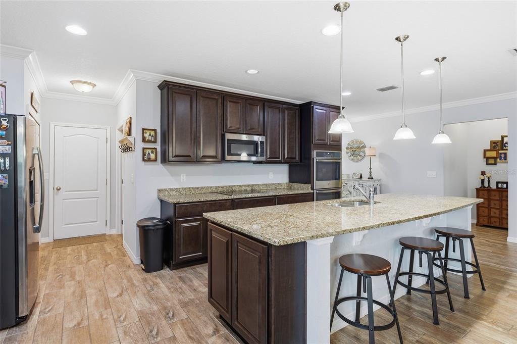 A kitchen features dark wood cabinets, granite countertops, a center island, and wood-look tile flooring — 186 FLATWOODS LOOP, DAVENPORT, FL