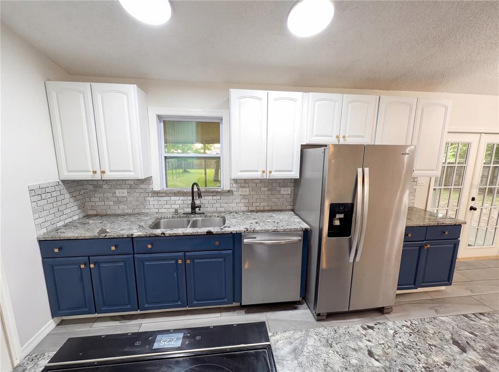 A kitchen features blue lower cabinets, white upper cabinets, granite countertops, and stainless steel appliances — 967 LAMPLIGHTER DRIVE NW, PALM BAY, FL