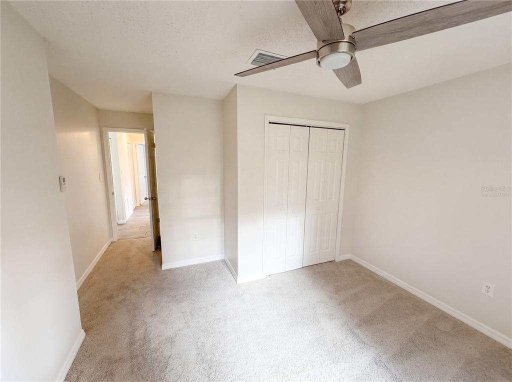 A bedroom with beige carpet, white walls, a ceiling fan, and a white closet — 967 LAMPLIGHTER DRIVE NW, PALM BAY, FL