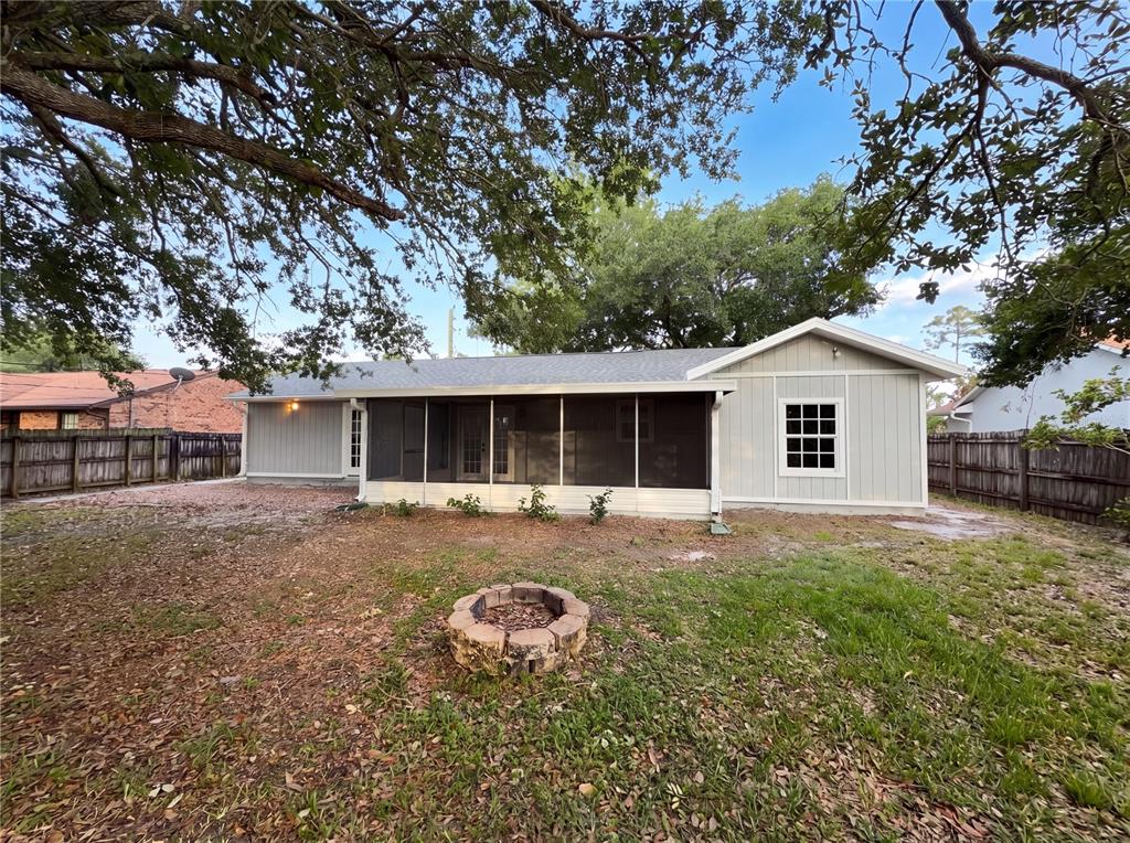 The exterior of a light-gray house features a screened-in porch and a stone fire pit — 967 LAMPLIGHTER DRIVE NW, PALM BAY, FL
