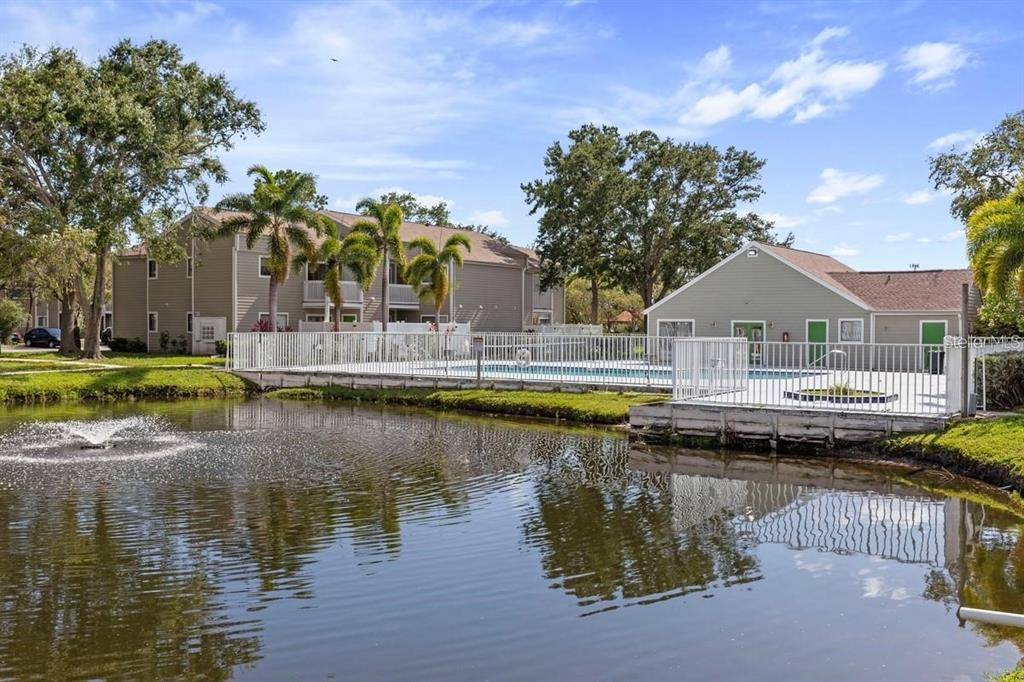 A pond with a fountain sits in front of an apartment complex and swimming pool — 7298 ULMERTON ROAD UNIT 602, LARGO, FL