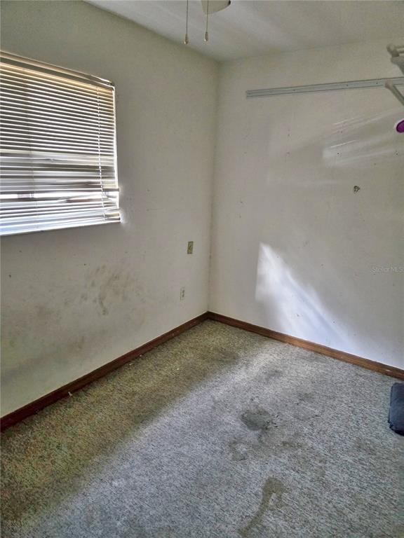 An empty room features a window with blinds, stained carpeting, and white walls — 5727 SW 10TH PLACE, GAINESVILLE, FL