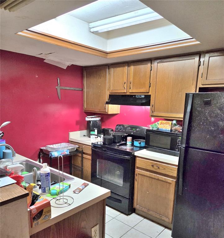 A kitchen with wood cabinets, red walls, a black stove, and a large ceiling skylight — 5727 SW 10TH PLACE, GAINESVILLE, FL