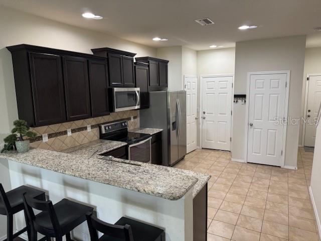 A kitchen features dark wood cabinets, granite countertops, stainless steel appliances, and tile flooring — 8723 TURNSTONE HAVEN PLACE, TAMPA, FL