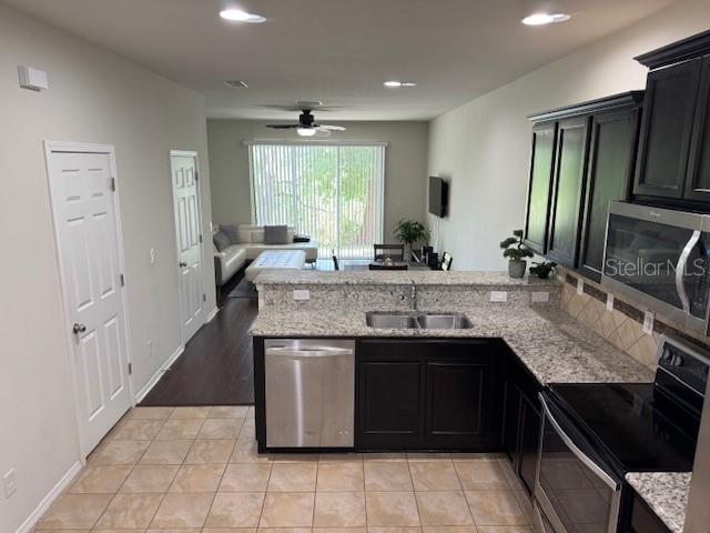 A kitchen with dark cabinets and granite countertops overlooks a living area with a ceiling fan — 8723 TURNSTONE HAVEN PLACE, TAMPA, FL