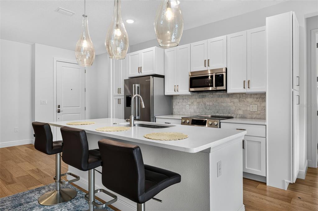 A modern kitchen features white cabinetry, stainless steel appliances, a quartz island, and three pendant lights — 600 3RD AVENUE S UNIT 207, ST PETERSBURG, FL
