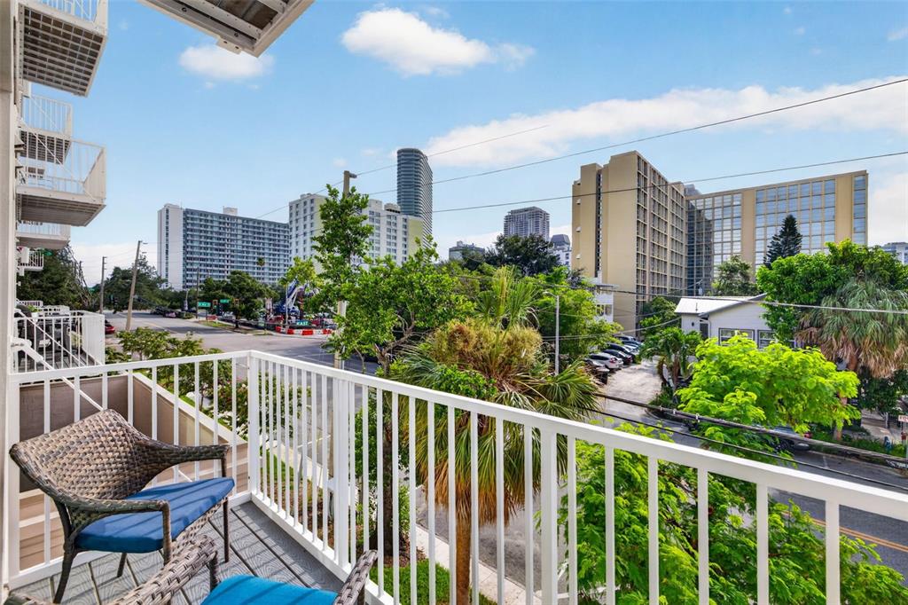 A balcony with a wicker chair overlooks a city street with trees and tall buildings — 600 3RD AVENUE S UNIT 207, ST PETERSBURG, FL