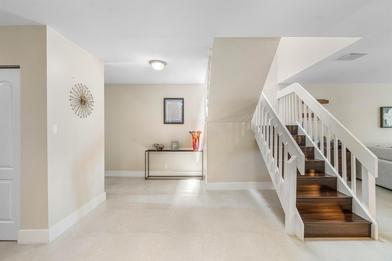 A bright entryway features light tile floors, a console table, and a wooden staircase — 6044 Glendale Drive, Boca Raton FL 33433, BOCA RATON, FL