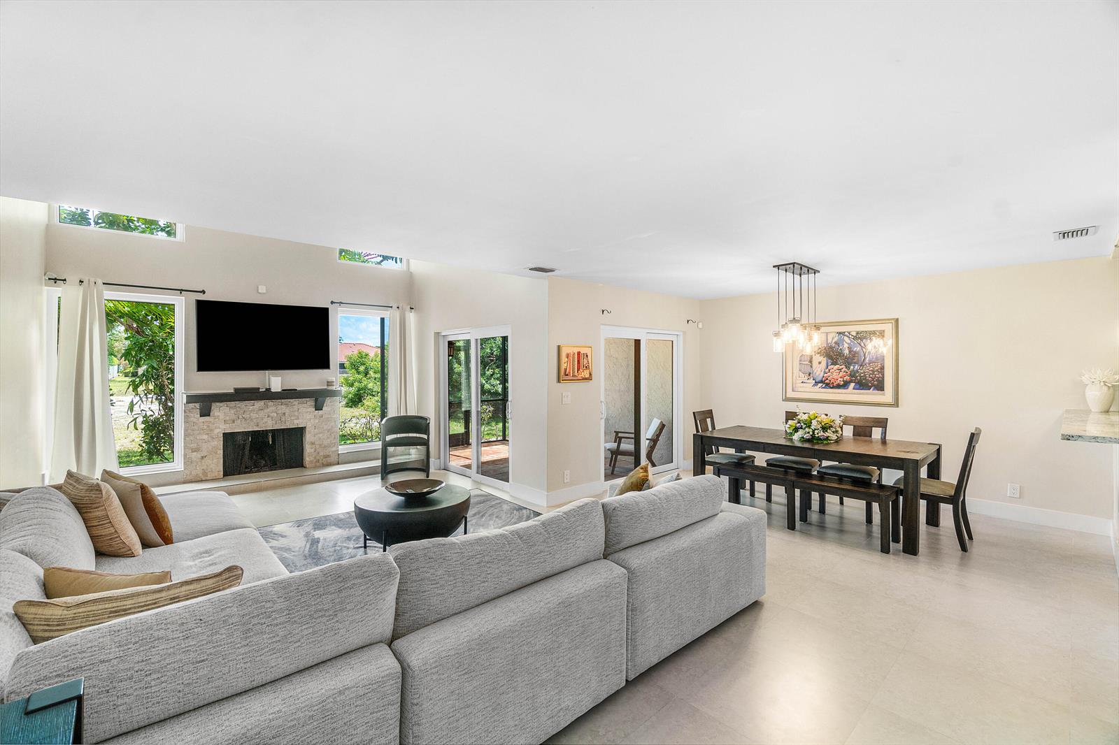 An open-concept living and dining area features a stone fireplace, gray sectional, and sliding doors — 6044 Glendale Drive, Boca Raton FL 33433, BOCA RATON, FL