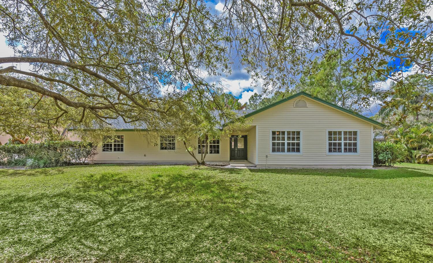 A single-story house with light siding and a large front lawn under a tree — 16244 E Downers Drive, Loxahatchee FL 33470, LOXAHATCHEE, FL