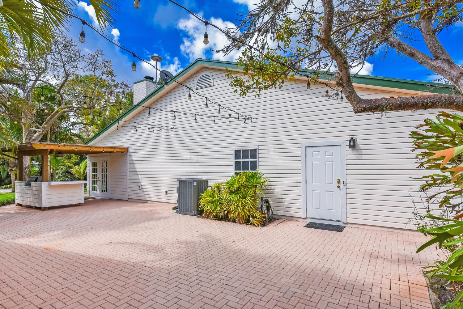 A paved patio area features a white house exterior, a small bar, and string lights — 16244 E Downers Drive, Loxahatchee FL 33470, LOXAHATCHEE, FL