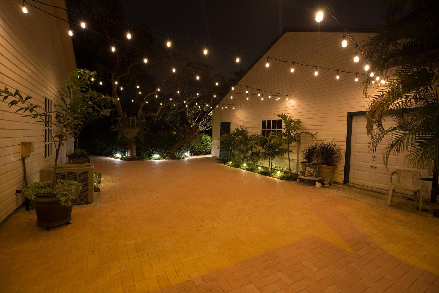 An outdoor brick patio at night illuminated by overhead string lights and landscape lighting — 16244 E Downers Drive, Loxahatchee FL 33470, LOXAHATCHEE, FL