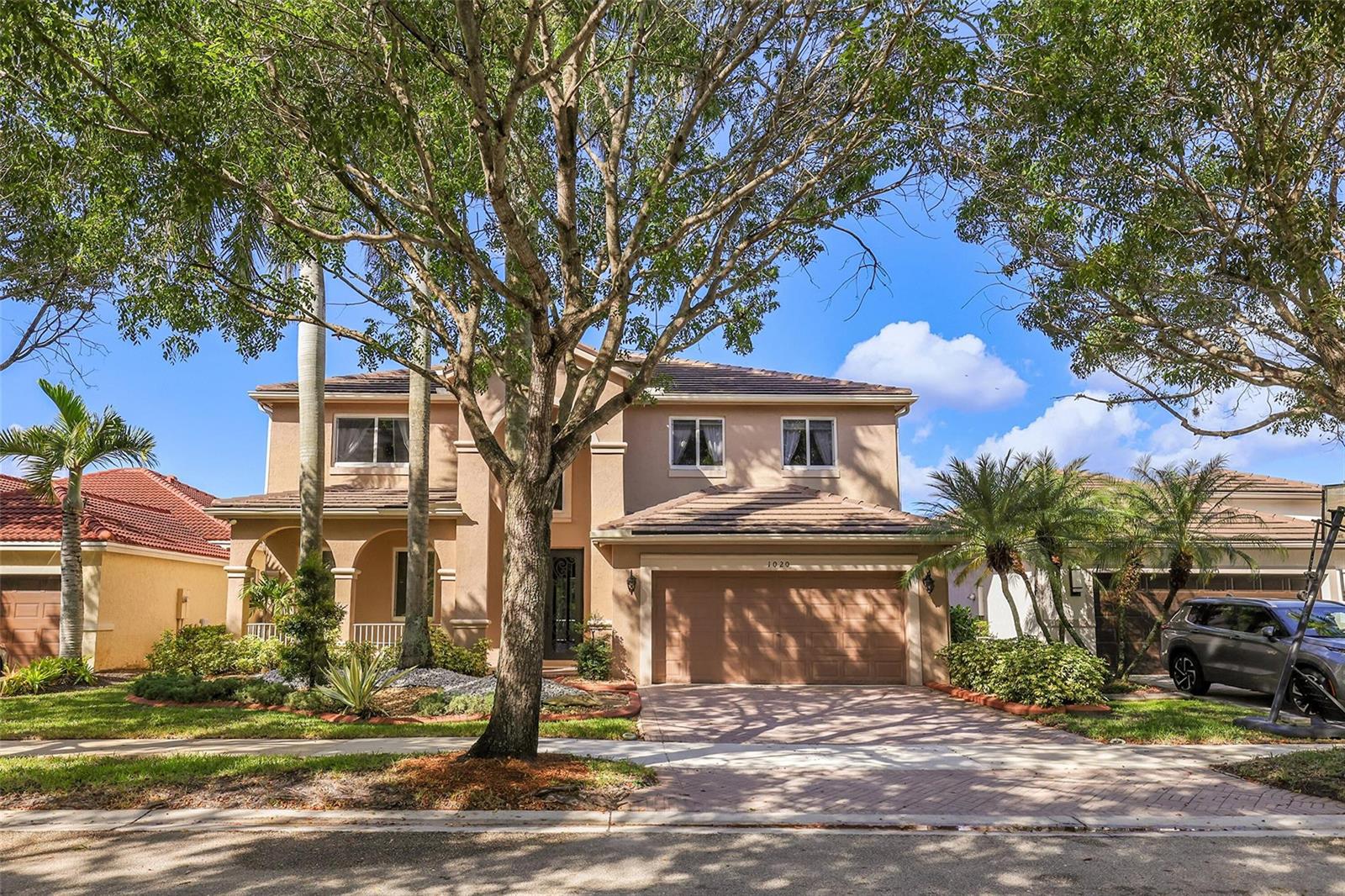 A two-story tan stucco house features a brown garage door and a brick paver driveway — 1020 Lavender Circle, Weston FL 33327, WESTON, FL