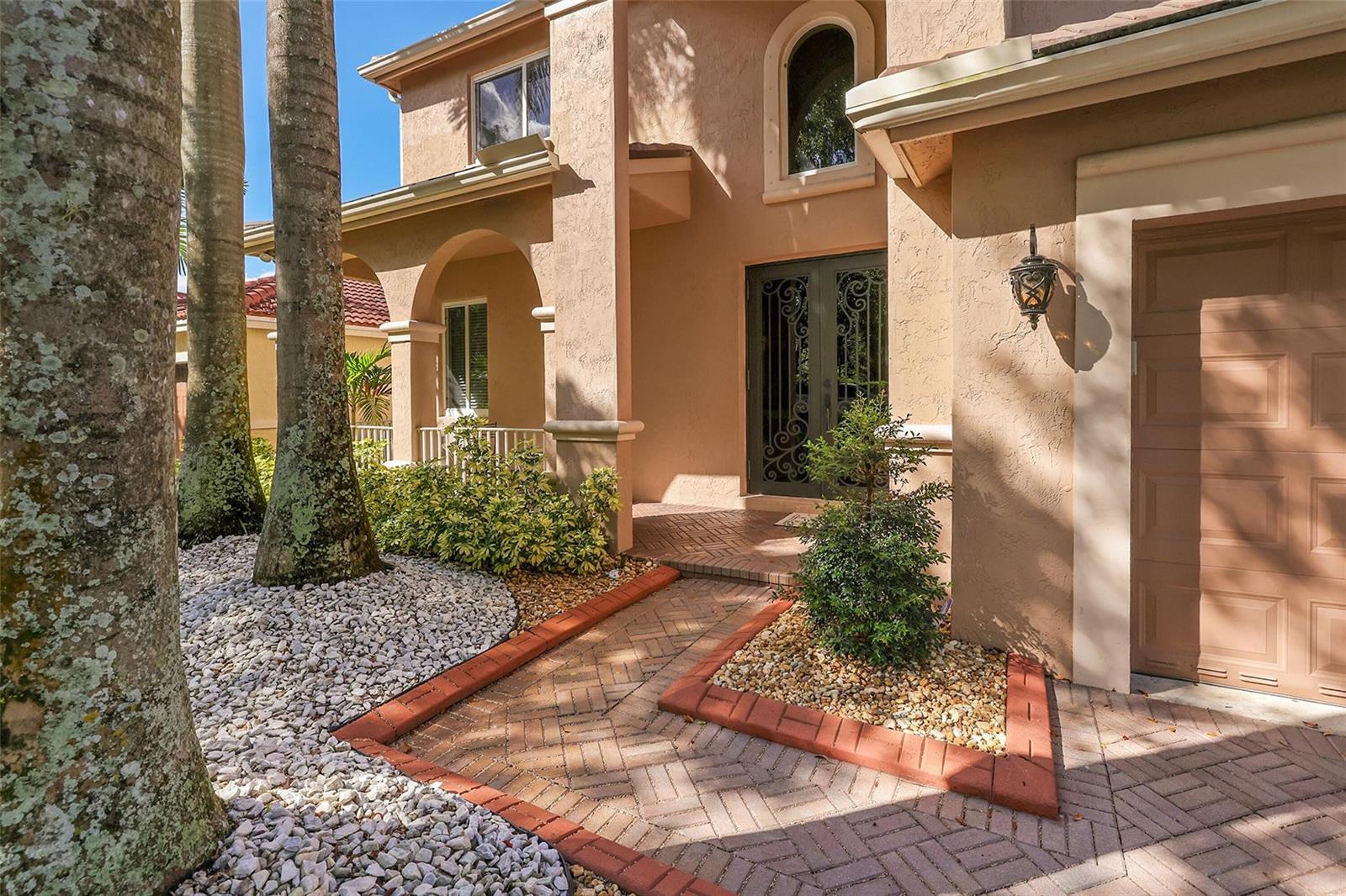 A tan two-story house features a brick walkway, palm trees, and a decorative metal front door — 1020 Lavender Circle, Weston FL 33327, WESTON, FL