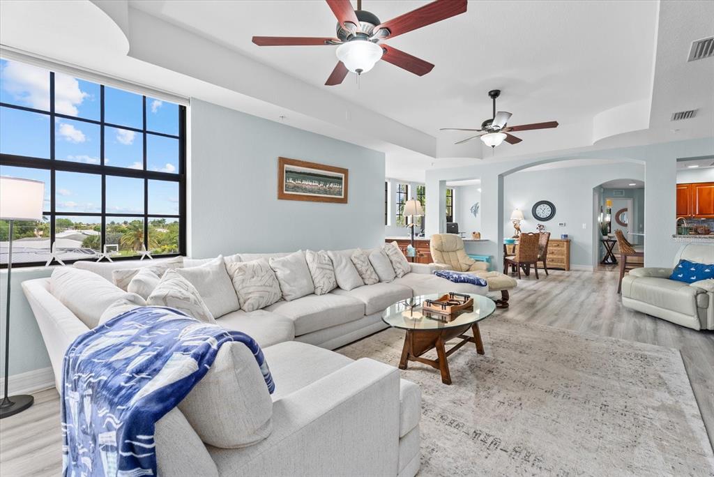 A spacious living room features a large sectional sofa, two ceiling fans, and expansive windows — 1349 AQUI ESTA DRIVE UNIT 136, PUNTA GORDA, FL