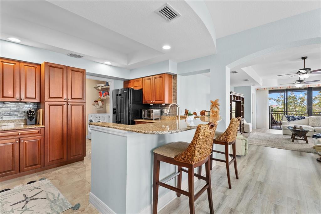 A kitchen with wood cabinets, granite countertops, and a breakfast bar overlooks a living area — 1349 AQUI ESTA DRIVE UNIT 136, PUNTA GORDA, FL