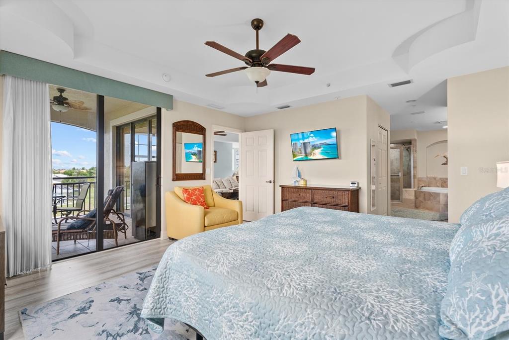 A bedroom features a coral-patterned bedspread, a yellow armchair, and a balcony with outdoor seating — 1349 AQUI ESTA DRIVE UNIT 136, PUNTA GORDA, FL