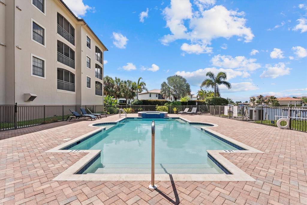 A rectangular swimming pool with a hot tub sits on a brick patio beside a building — 1349 AQUI ESTA DRIVE UNIT 136, PUNTA GORDA, FL