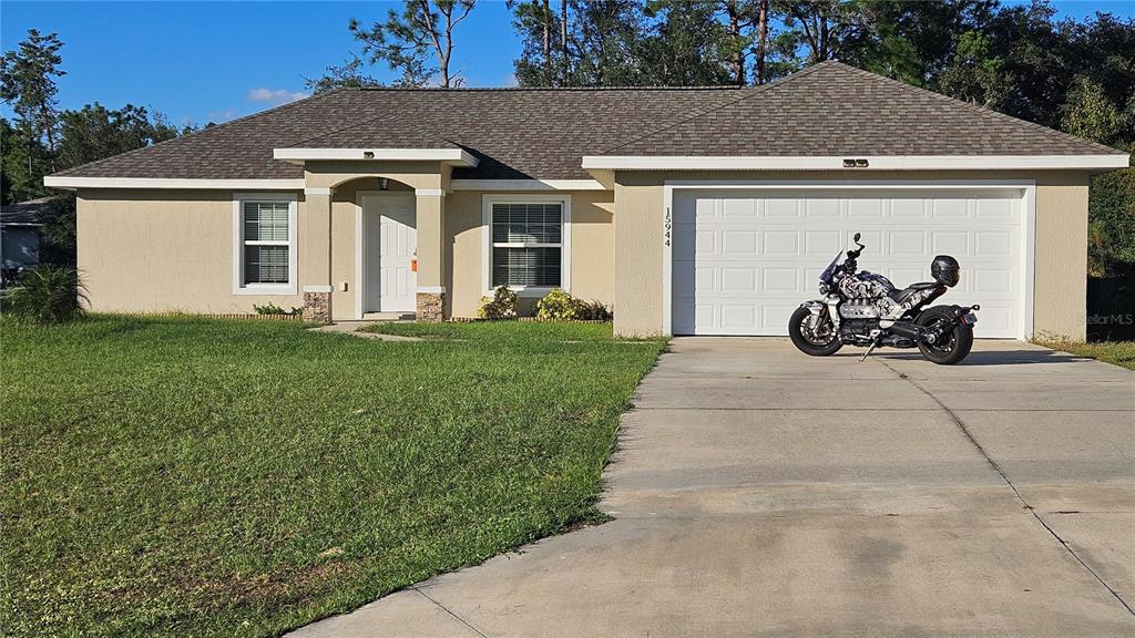 A single-story house with a tan stucco exterior, a two-car garage, and a motorcycle parked outside — 15944 SW 53RD COURT, OCALA, FL