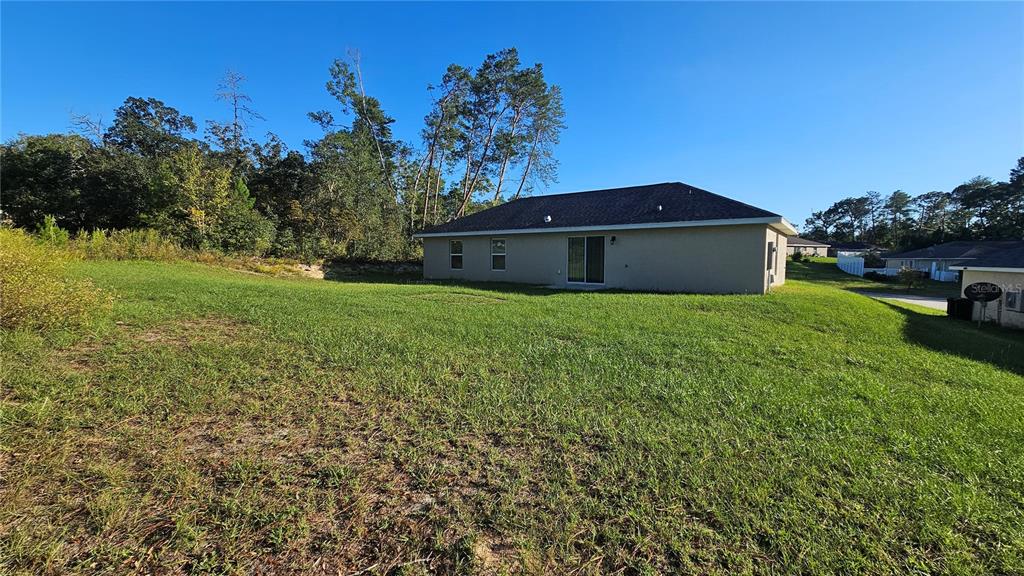 The exterior rear view of a single-story house features a grassy yard and trees — 15944 SW 53RD COURT, OCALA, FL