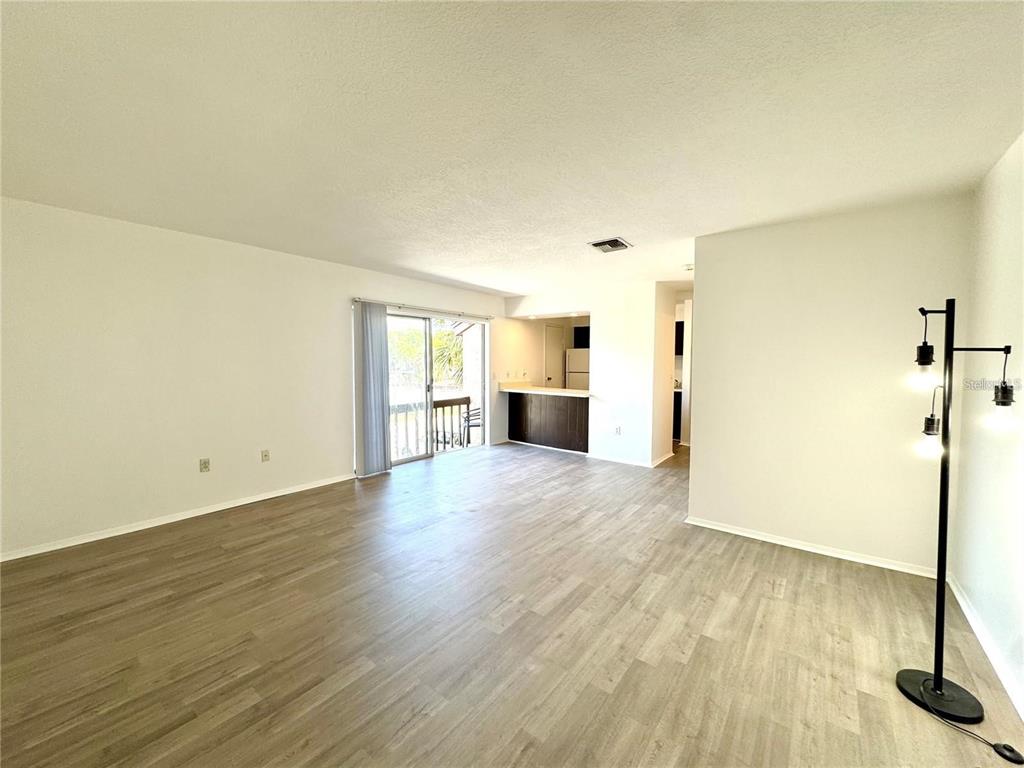 An open-concept living room features light wood-look flooring, white walls, and a sliding glass door — 2632 HIDDEN LAKE DRIVE N UNIT E, SARASOTA, FL