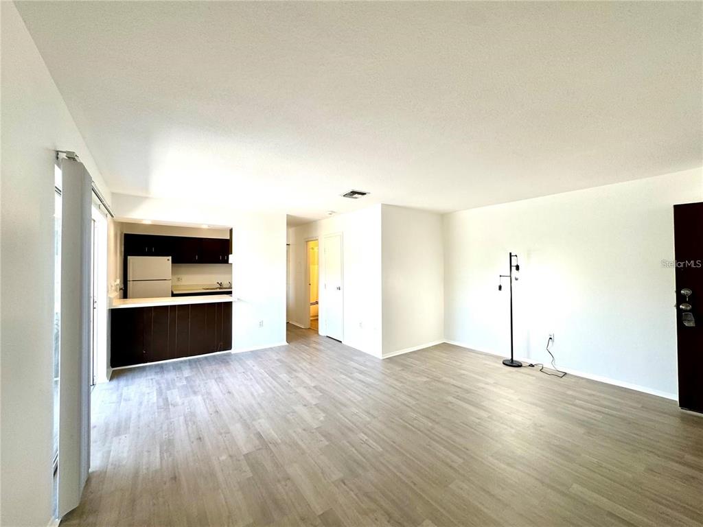 An open-concept living area features light wood-look flooring, white walls, and a kitchen with dark cabinets — 2632 HIDDEN LAKE DRIVE N UNIT E, SARASOTA, FL