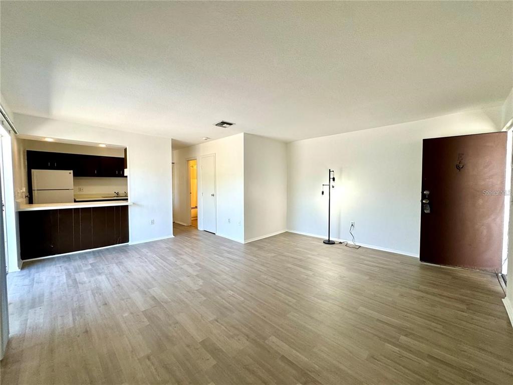 An open-concept living area features light wood-look flooring, white walls, and an adjacent kitchen — 2632 HIDDEN LAKE DRIVE N UNIT E, SARASOTA, FL