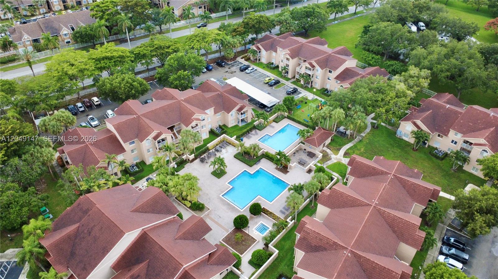 An aerial view shows apartment buildings with red roofs surrounding two swimming pools — 10521 SW 158th Ct # 203, Miami FL 33196, MIAMI, FL